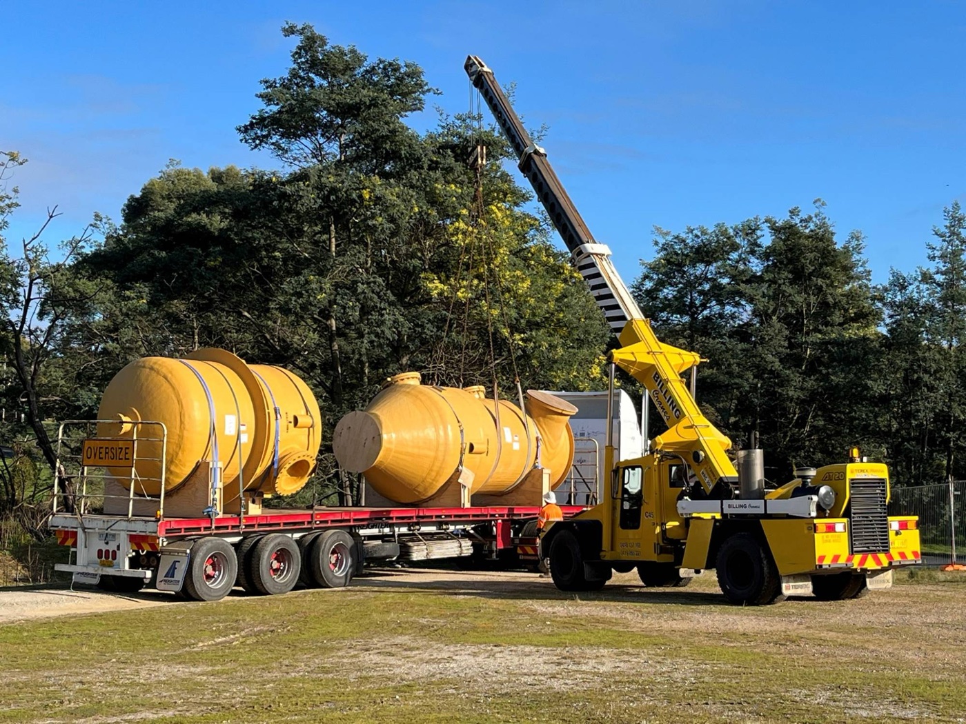 Two yellow FRP vessels on a truck being unloaded by crane
